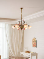 Clérachic chandelier lit beside cream curtains and a console with a gilt candle stand, with a plant branch at the left.