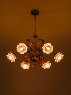 Clérachic rose chandelier glowing in a darkened room, its frosted glass roses lit amber and its ceramic roses in deep orange-pink.