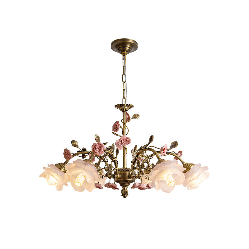 Clérachic chandelier on a white backdrop, with gold arms and leaves, pink ceramic roses and frosted glass rose shades lit warm white.