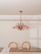 Clérachic rose chandelier with pale pink shades lit, hung in a white room with a low ceiling above a wooden dining table.