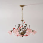 Clérachic chandelier with pink-tinted glass rose shades lit on a pale grey wall, its antique gold chain hung from a brass canopy.