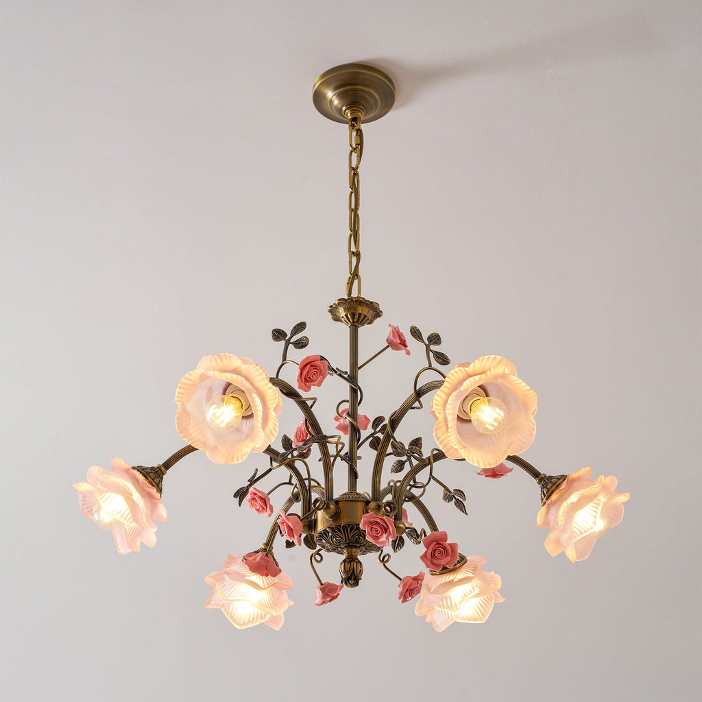 Clérachic chandelier with pink glass roses lit on a pale backdrop, seen from slightly below, with gold arms and pink ceramic roses.