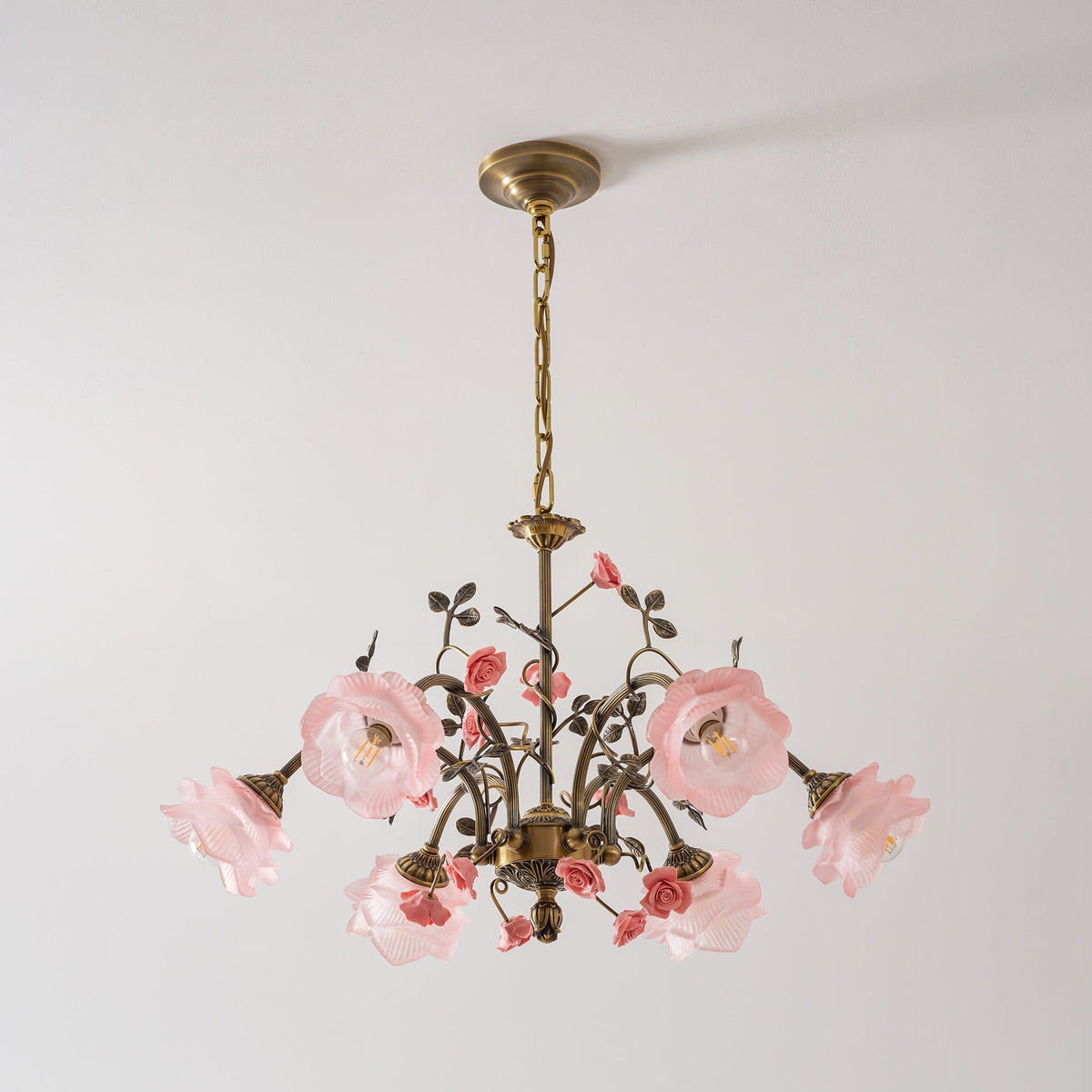Clérachic chandelier with glass roses at different angles, pink ceramic flowers and a ribbed gold centre, on a pale grey backdrop.