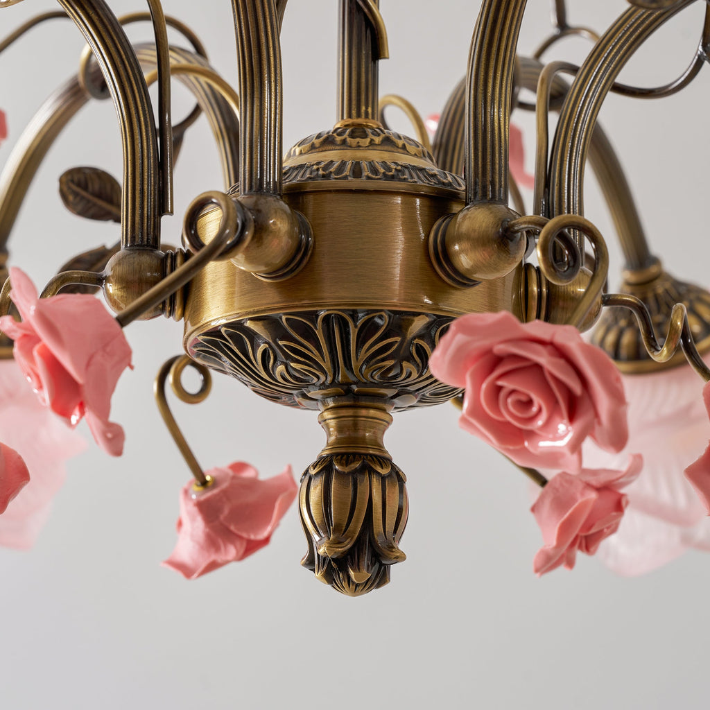 Close view of the carved gold centre of this Clérachic chandelier, with a bud finial and ceramic pink roses among the arms.