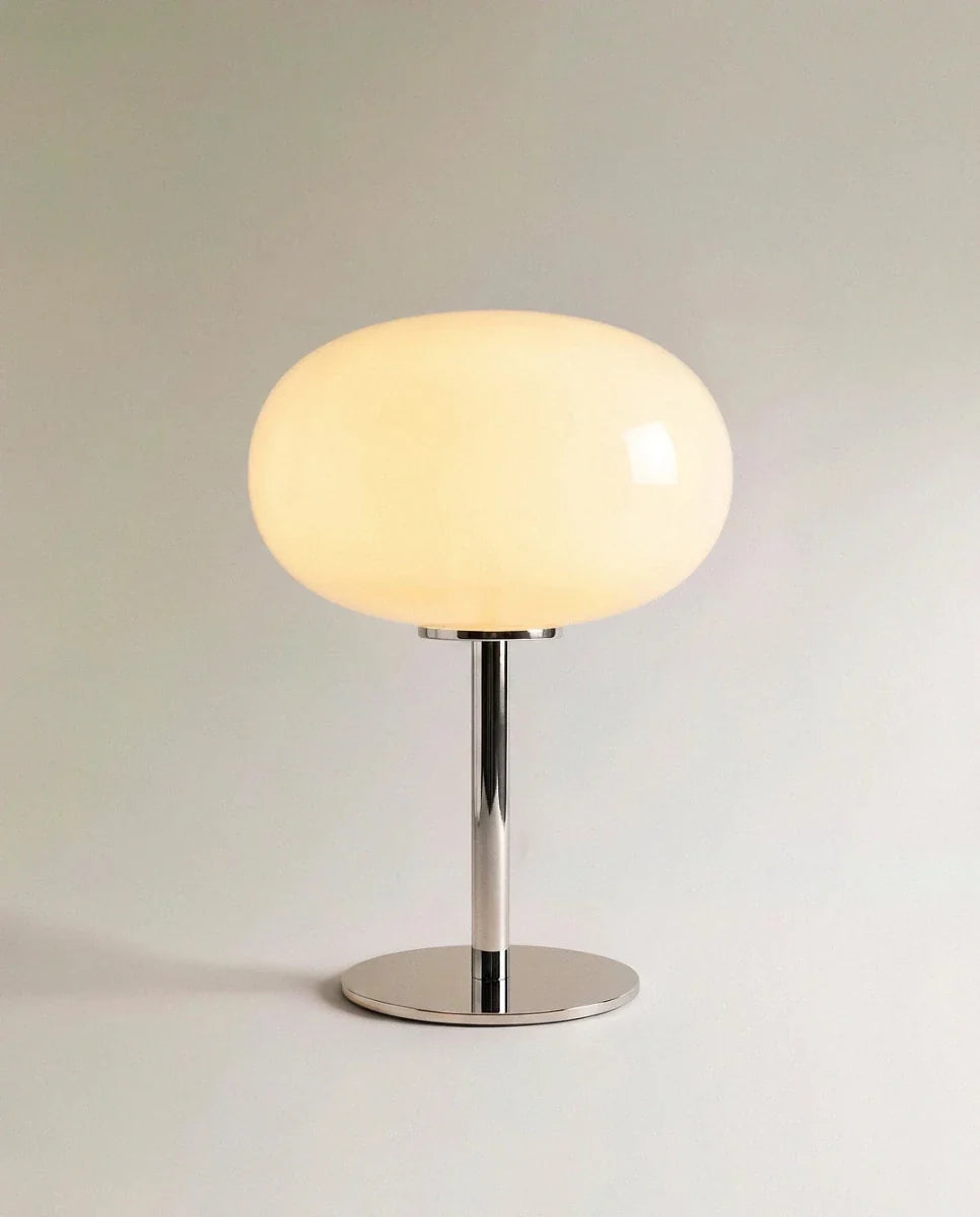 Clérachic opal glass table lamp with a glowing white globe shade on a slender chrome pedestal base.