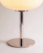 Clérachic table lamp in close detail, the chrome stem and round base beneath a glowing white glass shade.