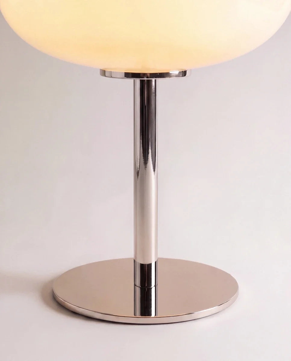 Clérachic table lamp in close detail, the chrome stem and round base beneath a glowing white glass shade.
