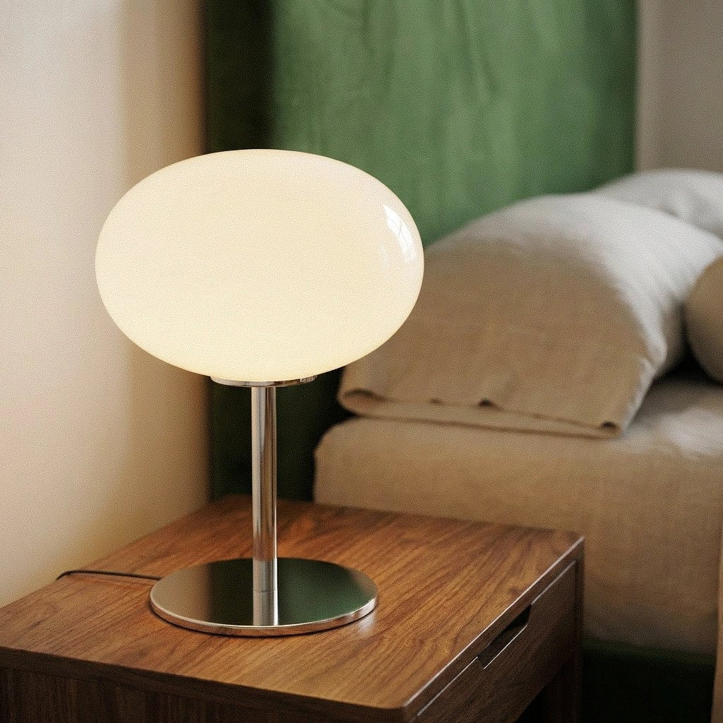 Clérachic globe table lamp lit on a burl-wood nightstand in a green bedroom, beside a small vase of flowers.