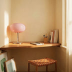 Clérachic pink glass globe table lamp glowing on a wood desk nook beside a stack of books at sunset.