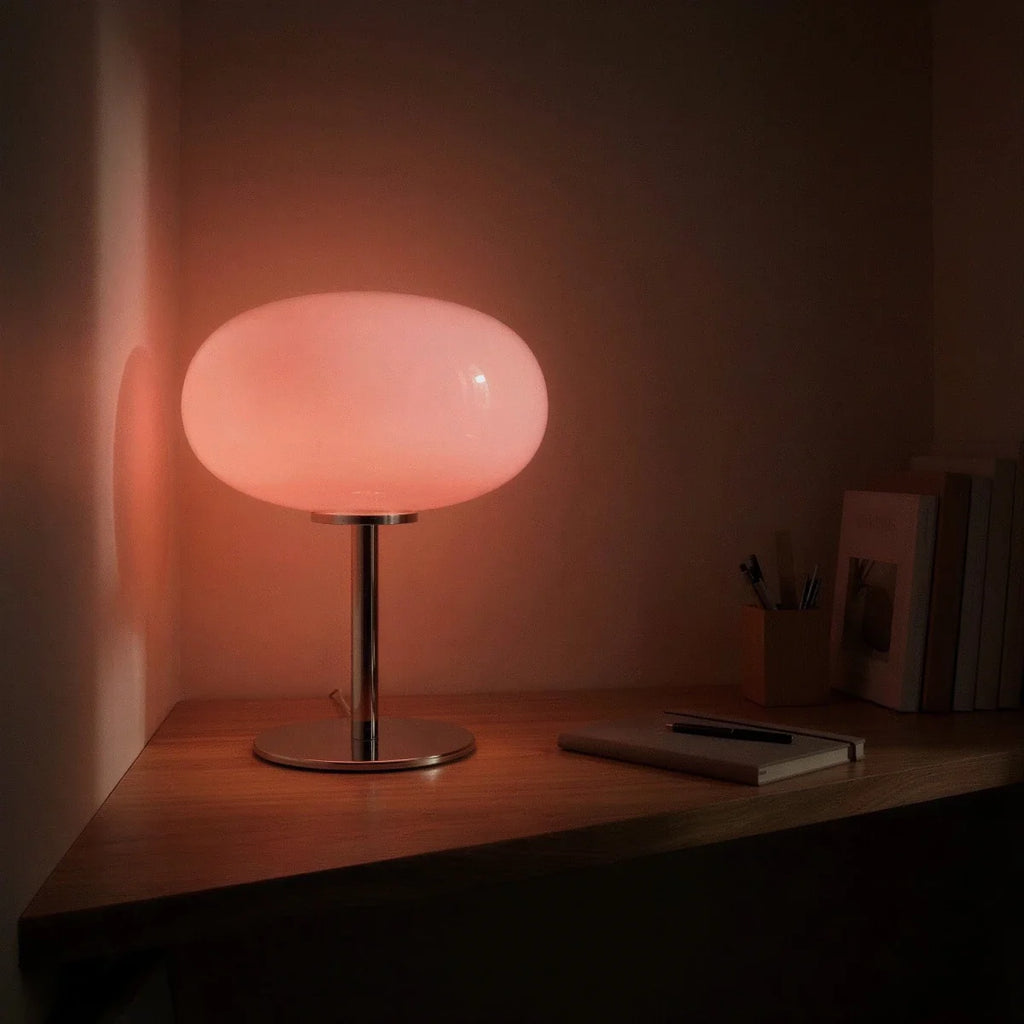 Clérachic pink glass globe table lamp glowing softly on a dark wood desk beside a notebook at night.
