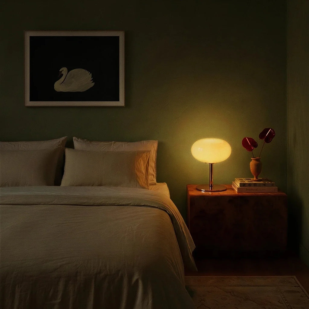 Clérachic globe table lamp glowing on a walnut nightstand in a green bedroom beneath a framed swan print.