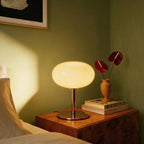 Clérachic globe table lamp glowing on a burl-wood nightstand beside a vase of red anthurium flowers.