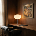 Clérachic globe table lamp glowing on a walnut desk in a wood-paneled study beside a framed painting.