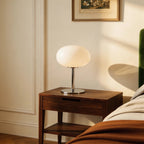 Clérachic globe table lamp glowing on a walnut nightstand beside a bed with a green velvet headboard.