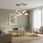 A Clérachic water-lily pendant cluster hangs high in a sage-green living room, with a low media unit and a framed lily-pad print on the wall.