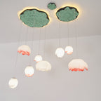 Pink-tipped and white water-lily pendants from Clérachic hang on thin cords beneath two green lily-pad canopies, against a pale wall.