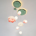 Looking up at the Clérachic water-lily pendants, with pink-tipped and white buds on cords of different lengths below green lily-pad plates.