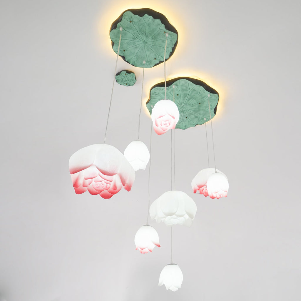 The Clérachic water-lily pendant cluster lit against a white wall, with the buds glowing white and coral beneath glowing lily-pad canopies.