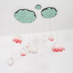 Straight-on view of a Clérachic water-lily pendant cluster on a white wall, with pink-tipped buds hanging below two green lily-pad canopies.