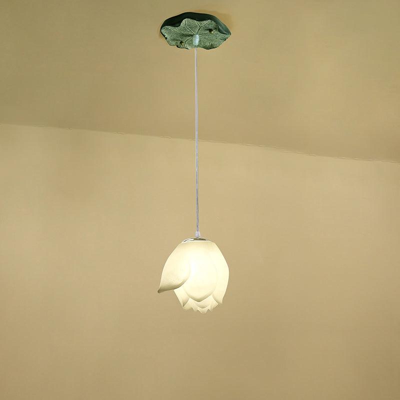 A single Clérachic water-lily pendant in a pale white bud shape hangs on a thin cord from a small green lily-pad canopy, against a warm cream wall.