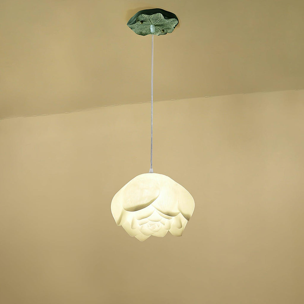 A single Clérachic water-lily pendant with a wider white bloom, hanging on a thin cord from a small green lily-pad canopy against a cream wall.