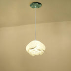 A single Clérachic water-lily pendant with a wider white bloom, hanging on a thin cord from a small green lily-pad canopy against a cream wall.