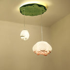 Two Clérachic water-lily pendants, a small white bud and a wider bloom, hang from a green lily-pad canopy with a warm glow behind it.