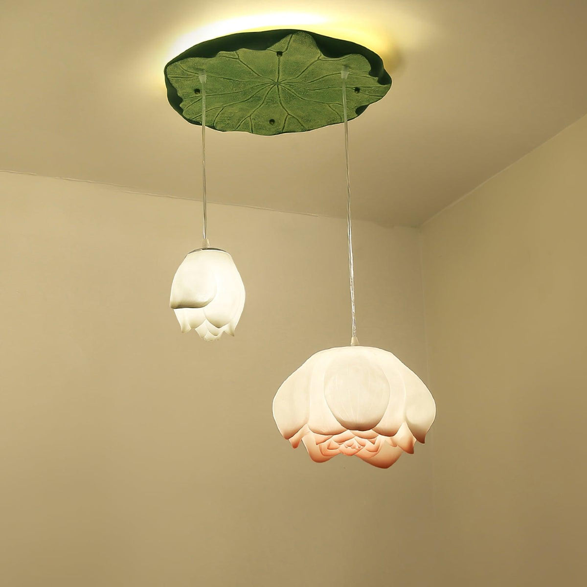 Two Clérachic water-lily pendants, a small white bud and a wider bloom, hang from a green lily-pad canopy with a warm glow behind it.