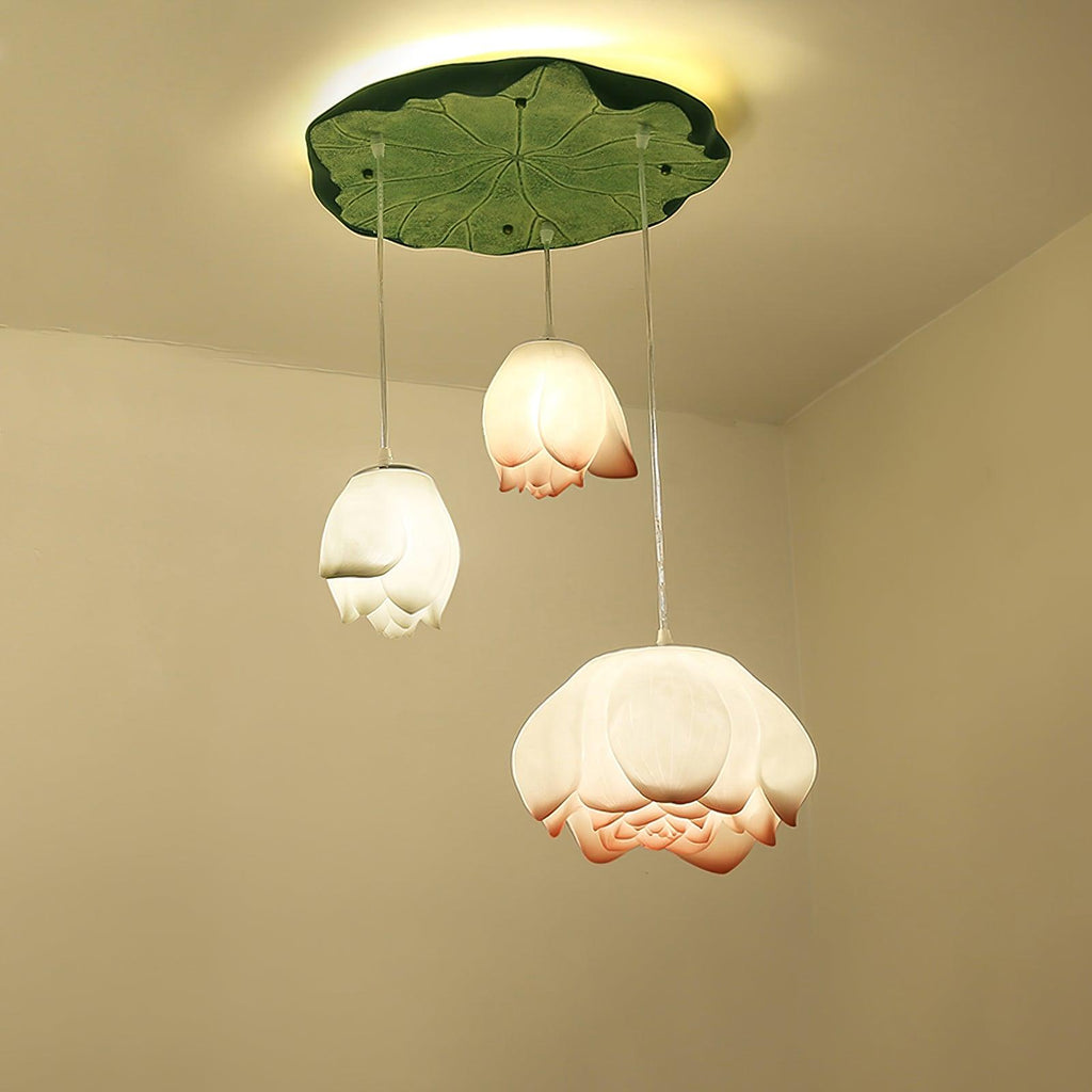 Three Clérachic water-lily pendants, with white and coral-tipped blooms, hang from a green lily-pad canopy against a warm cream corner.