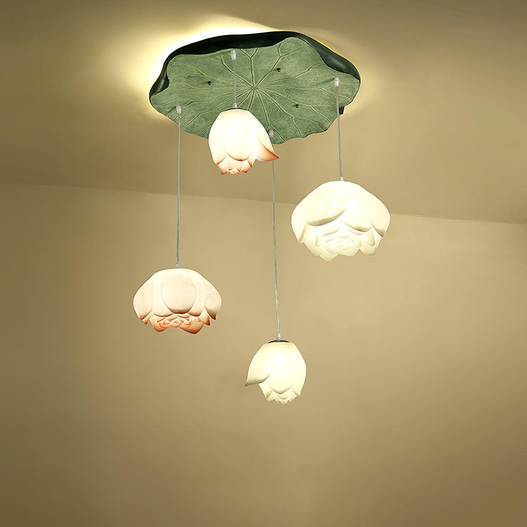 Four lit Clérachic water-lily pendants of different sizes hang from one wide green lily-pad canopy, with a warm halo behind it.