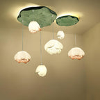 Six Clérachic water-lily pendants hang from a larger green lily-pad canopy with a smaller one beside it, glowing warm against a cream corner.