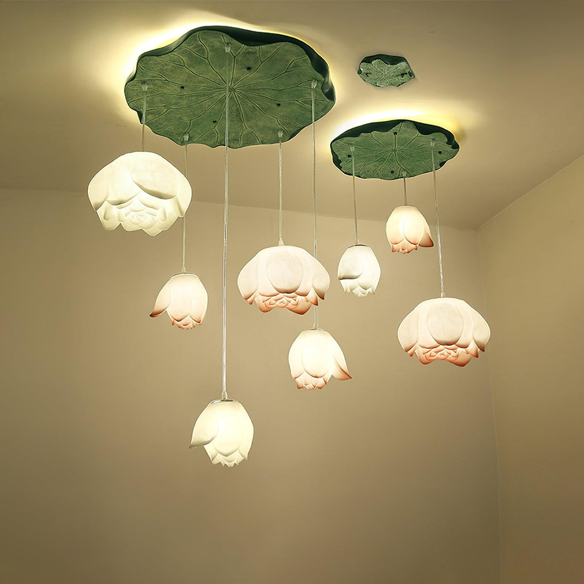 Seven Clérachic water-lily pendants hang at varied heights beneath a large and a small green lily-pad canopy, glowing warm in a cream corner.