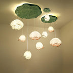 Looking up at a full Clérachic water-lily pendant cluster, the white and coral-tipped buds glow beneath lily-pad canopies against a cream wall.