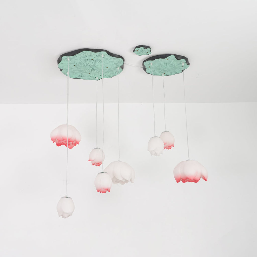 The Clérachic water-lily pendants hang on a white ceiling, with pink-tipped buds on long cords under two lily-pad canopies.