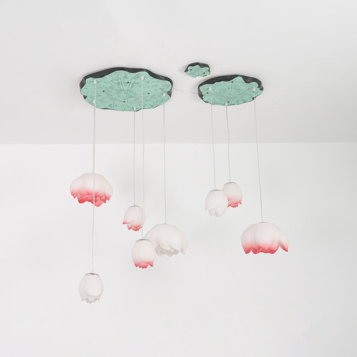 The Clérachic water-lily pendants hang on a white ceiling, with pink-tipped buds on long cords under two lily-pad canopies.