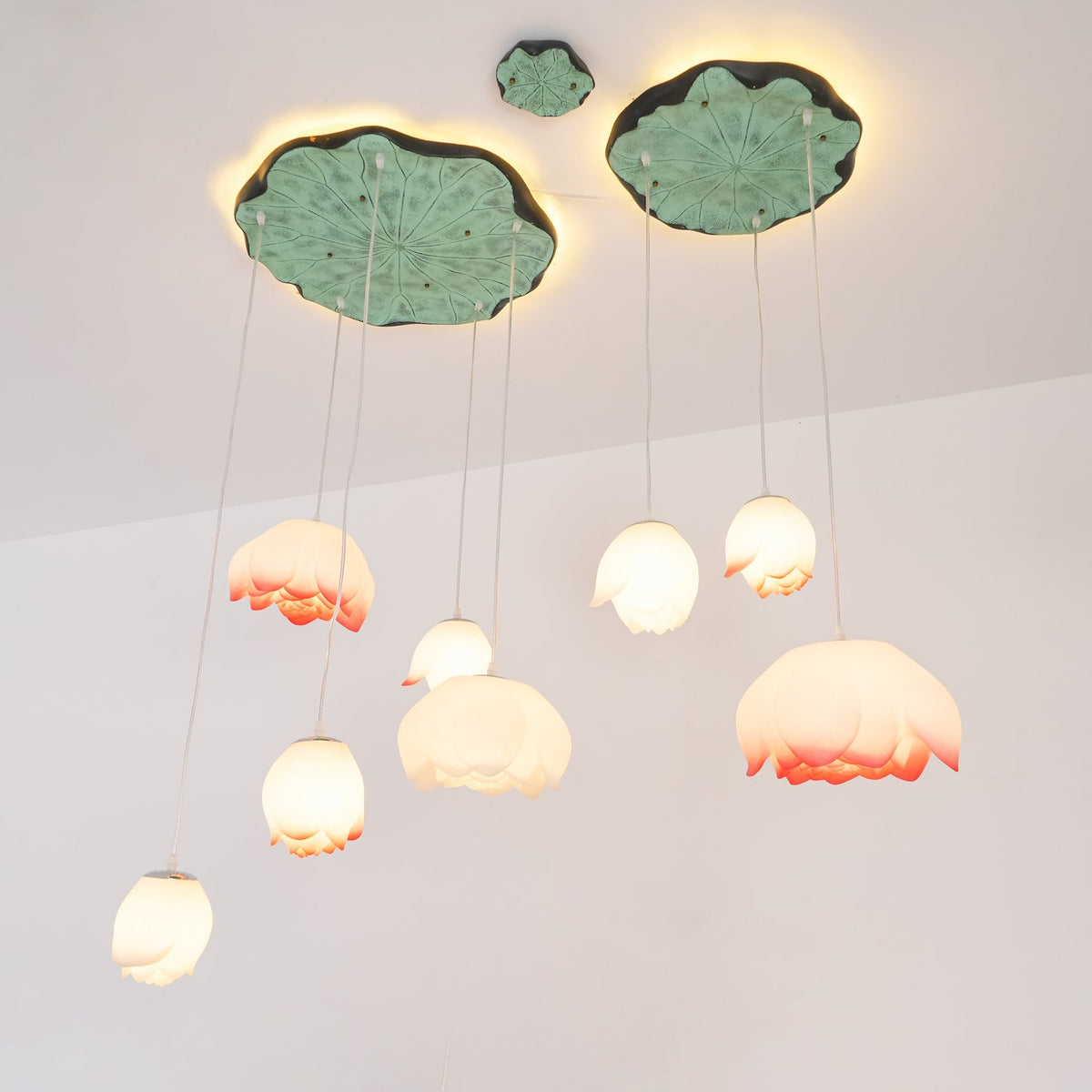 Looking up at the Clérachic water-lily pendants, pink-tipped and white buds hang at varied heights beneath two glowing lily-pad canopies.
