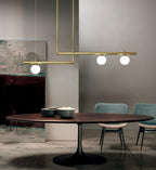 Clérachic gold pendant with offset bars and three glowing globes above a round walnut table, with teal chairs and a large painting.