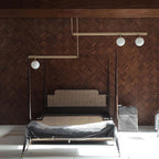 Clérachic gold pendant with three globes hanging in front of a herringbone timber wall, over a bed with a rattan headboard.