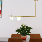 Clérachic two-globe gold pendant bar over a dining table, with a peace lily in a pot and tan leather chairs below.