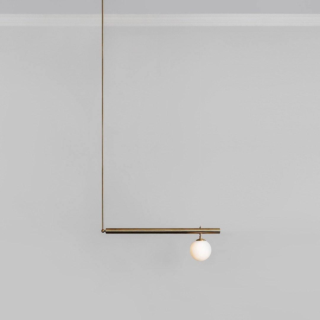 Single-globe Clérachic pendant on a plain grey background, with a long gold rod and one short bar holding an opal globe.