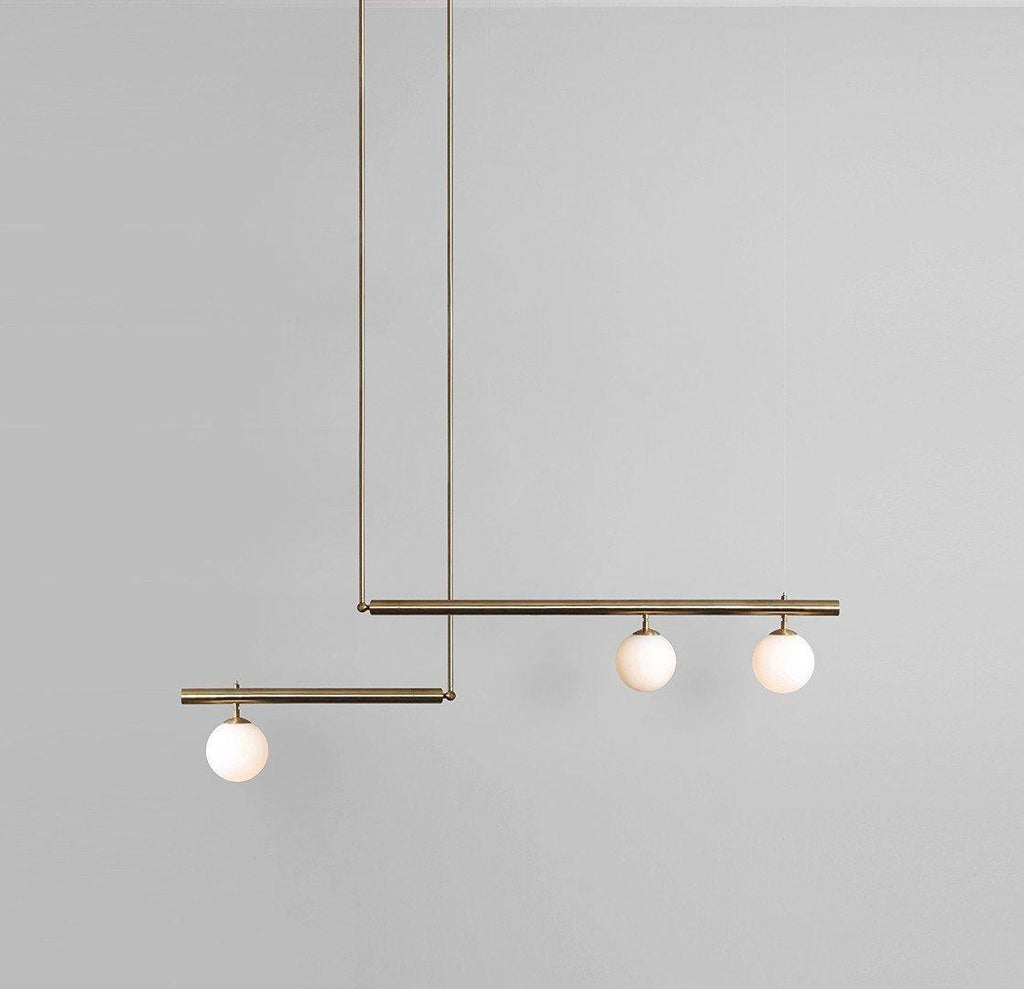 Clérachic gold pendant with three opal globes on two offset bars, hanging against a plain grey wall.