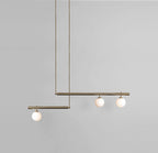 Clérachic gold pendant with three opal globes on two offset bars, hanging against a plain grey wall.