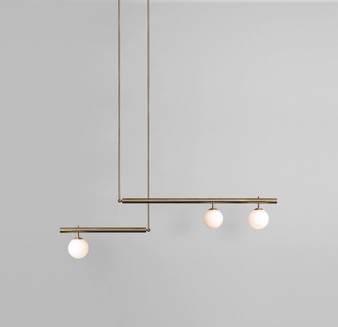 Clérachic gold pendant with three opal globes on two offset bars, hanging against a plain grey wall.