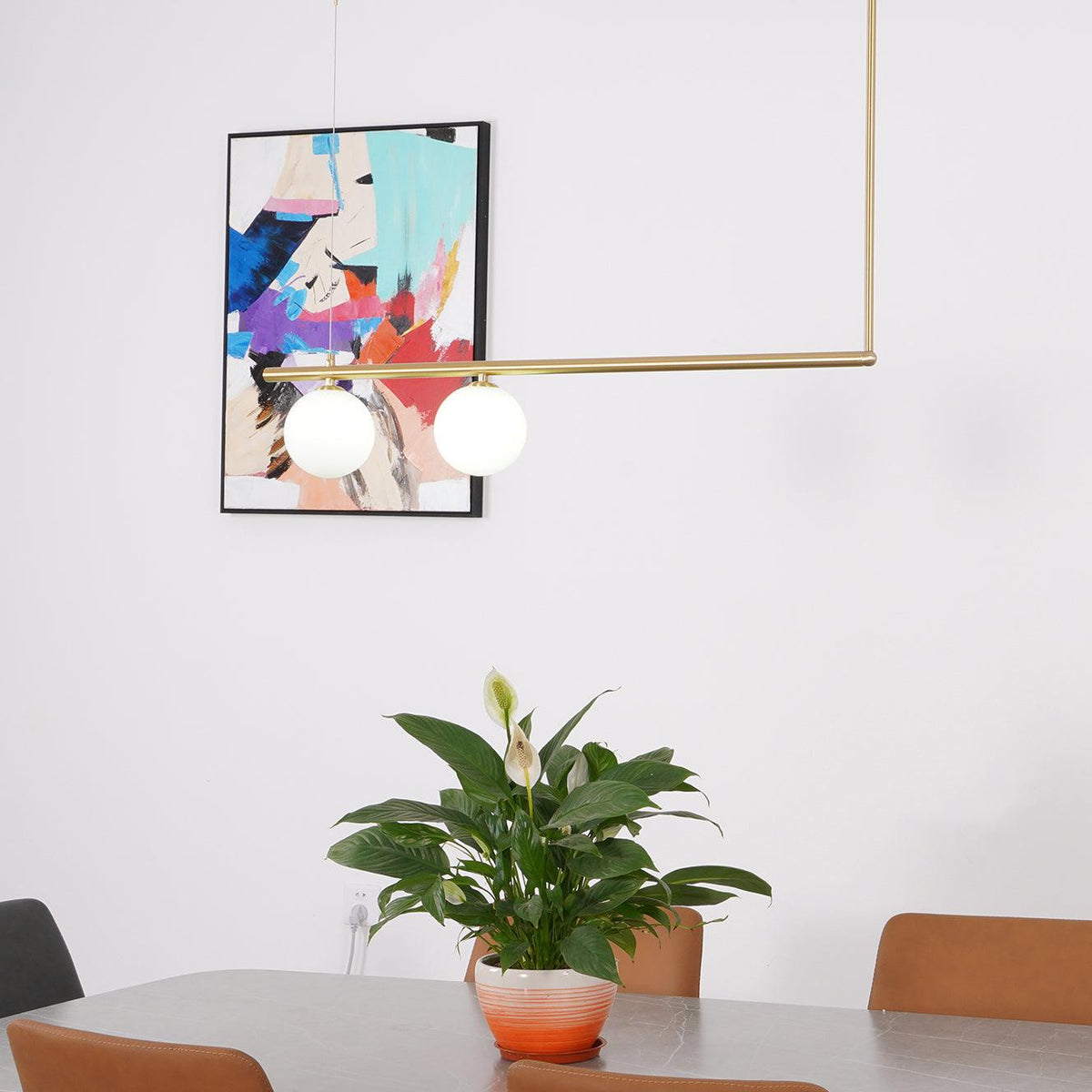 Clérachic two-globe gold pendant above a dining table with a flowering plant, in front of a colourful abstract print.