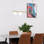 Clérachic gold pendant bar with two opal globes hanging in front of a bright abstract print, above a table with a plant.