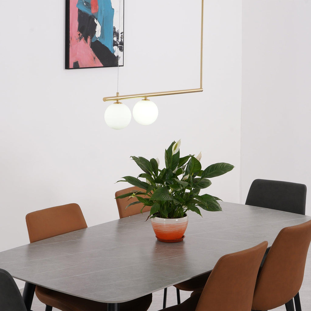 Two opal globes on a gold Clérachic pendant bar, hung over a dining table with a peace lily and tan chairs.