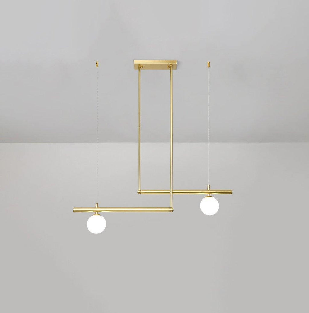 Clérachic gold pendant with two globes on offset bars, hanging from a ceiling plate against a pale grey wall.