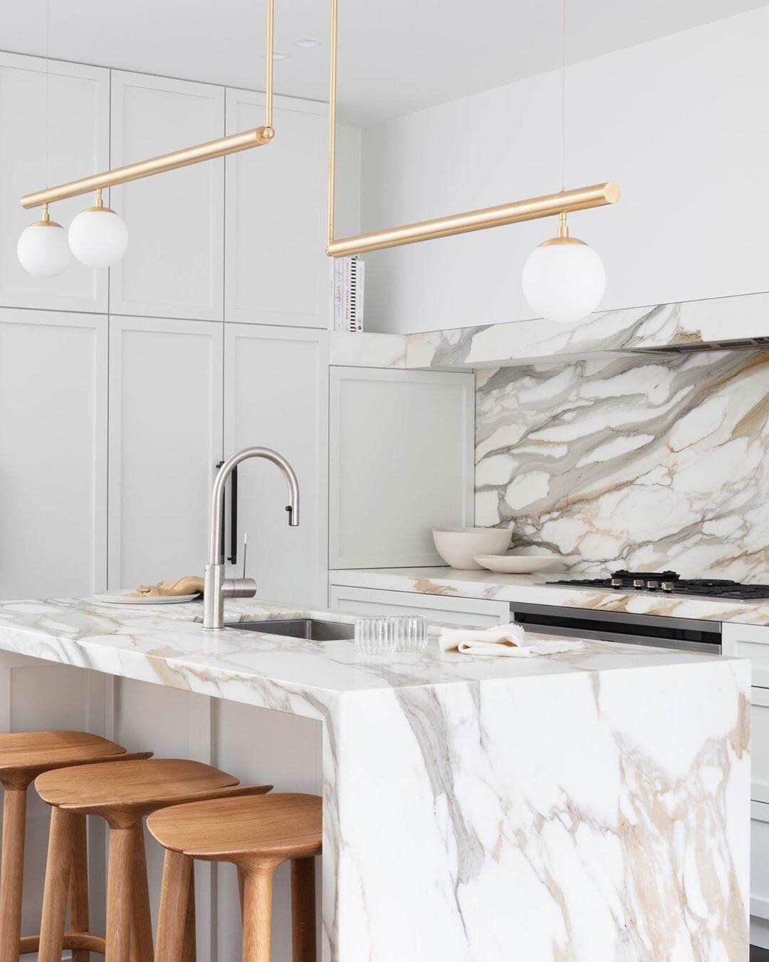 Clérachic gold pendant with three globes over a marble-topped kitchen island, with timber stools and a tall faucet.