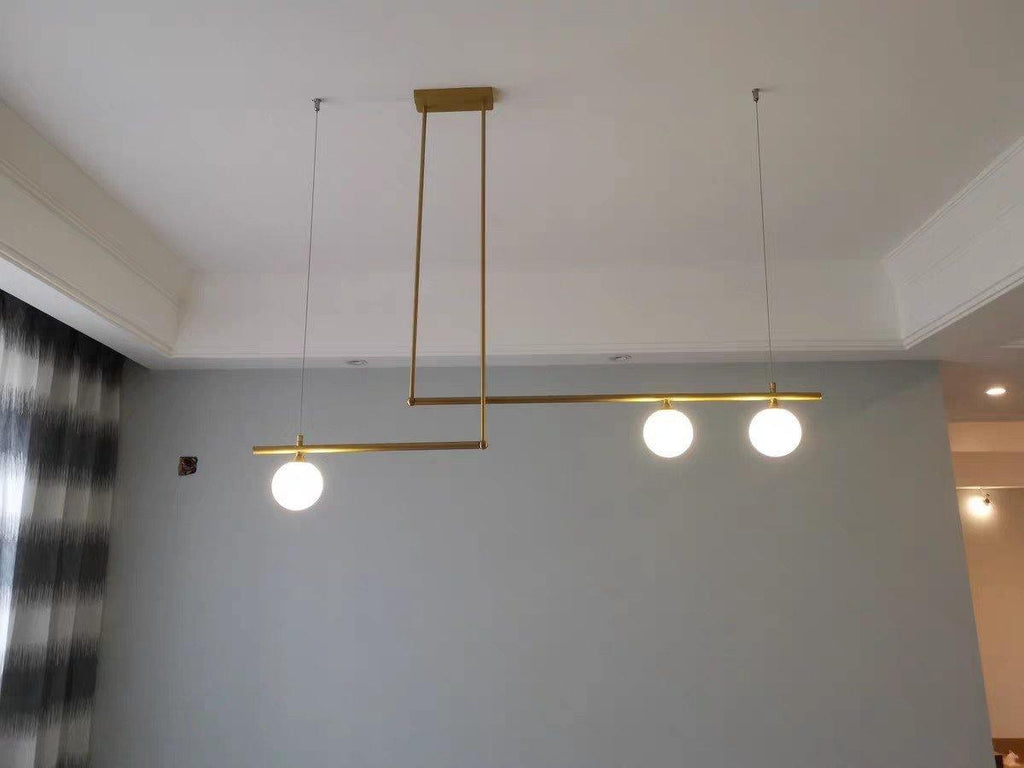 Clérachic gold pendant with three glowing globes hanging from a recessed ceiling in a room with a grey wall.