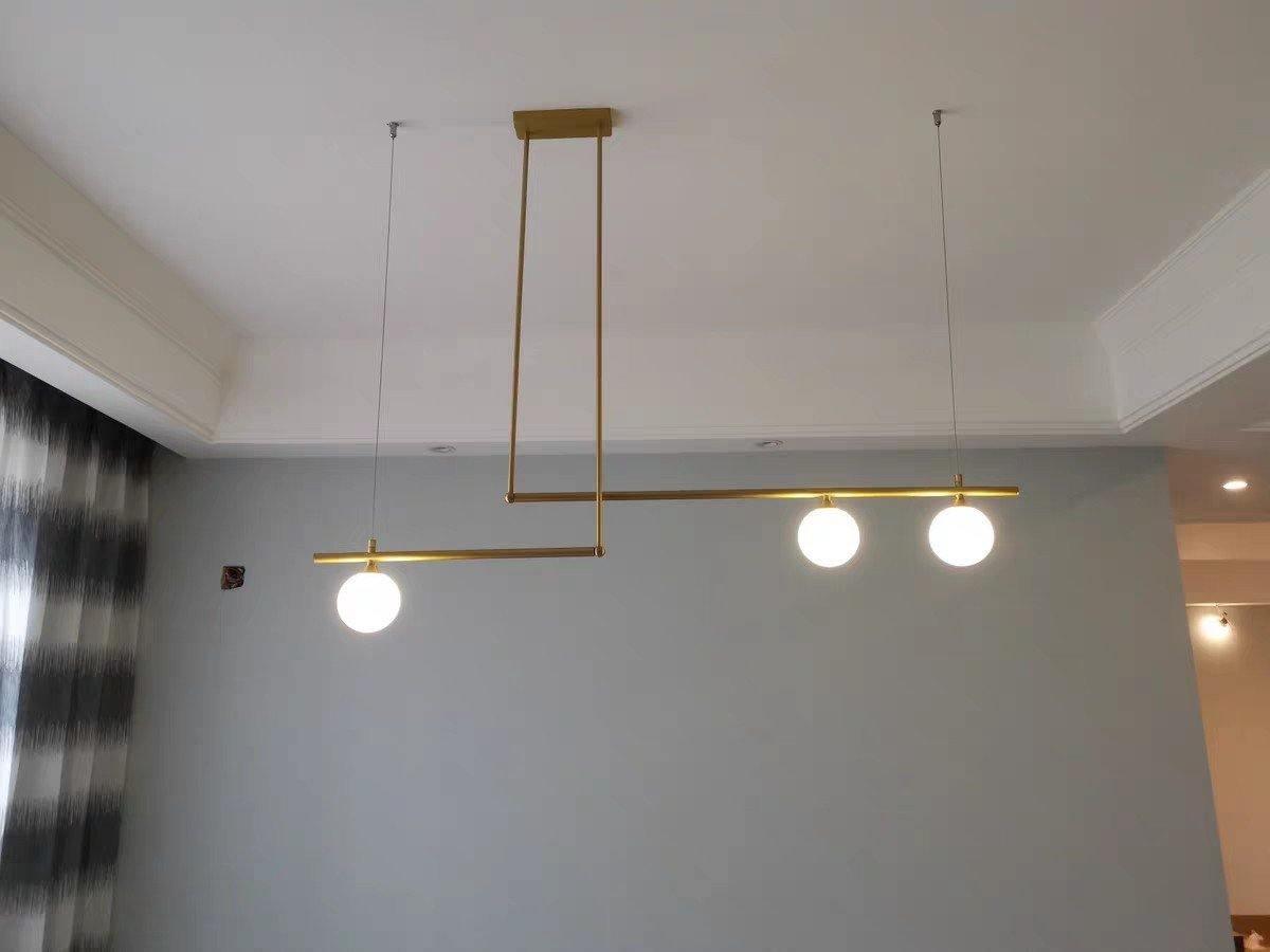 Clérachic gold pendant with three glowing globes hanging from a recessed ceiling in a room with a grey wall.